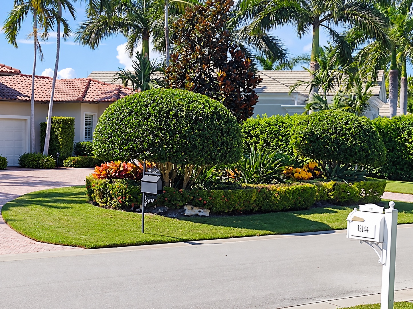 Carefully shaped shrubs, colorful planting beds, and tropical palms surrounded by a neatly maintained lawn